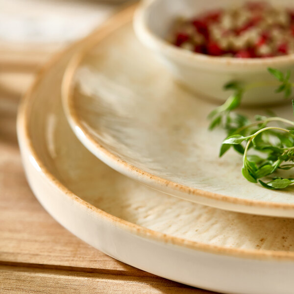 A round beige porcelain deep coupe plate with a slightly rustic edge.