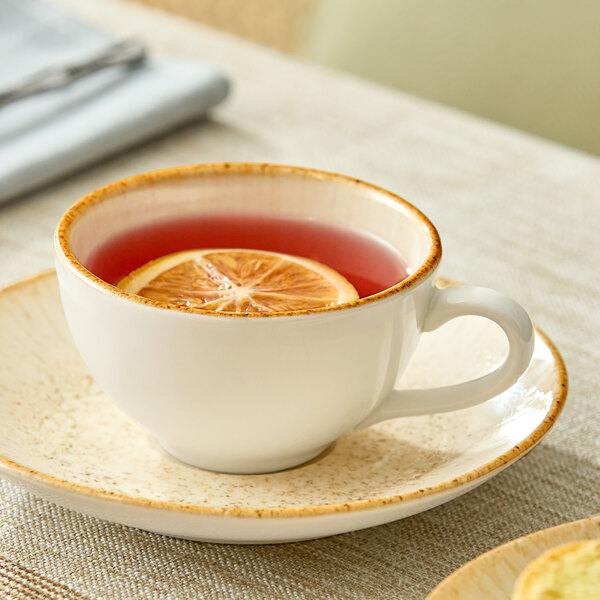 A beige porcelain cup filled with a reddish beverage and a lemon slice, placed on a matching saucer.