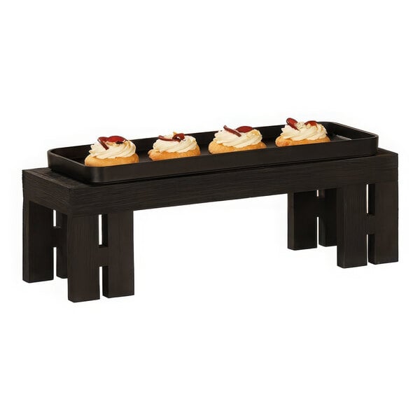A rectangular black wood display riser with frosted cupcakes on a table.
