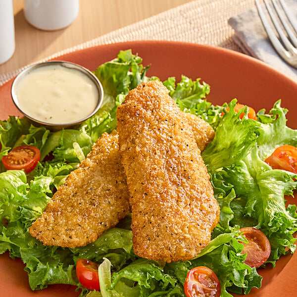 A plate of Mrs. Friday's Parmesan Crusted Pollock fish fillets with salad on a table.
