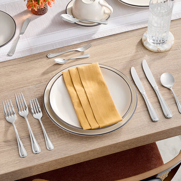 A table setting with an Acopa Edgeworth stainless steel dinner spoon on a white plate with napkins.