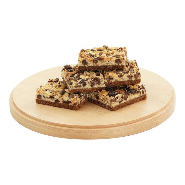 A stack of brownies with nuts on top on a wooden plate.