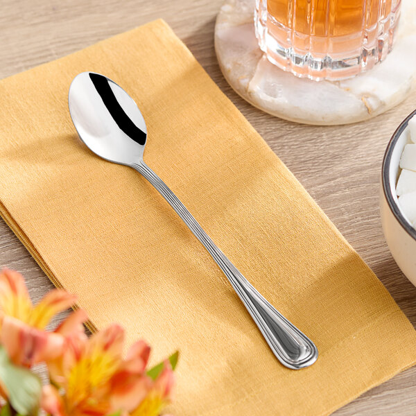 An Acopa Edgeworth stainless steel iced tea spoon on a napkin next to a glass of tea.
