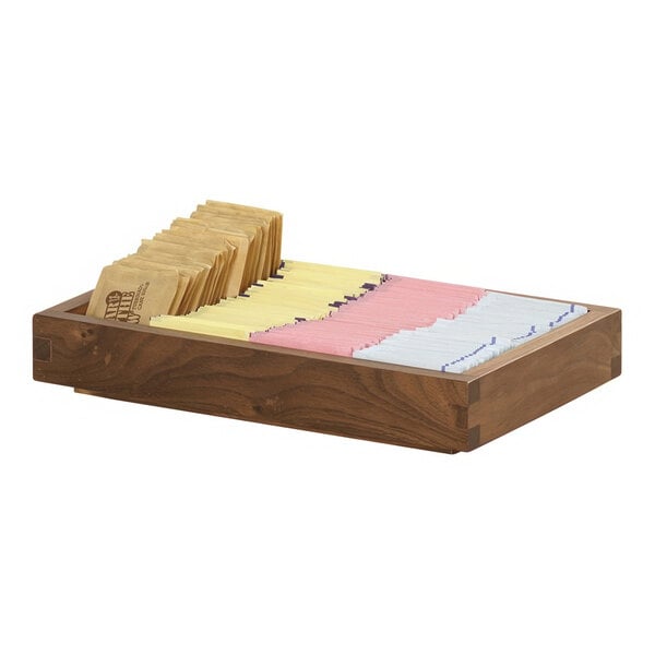 A wooden box with several different colored packets of tea on a table in a bakery display.