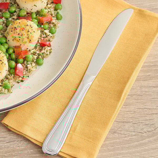 An Acopa stainless steel table knife on a plate of scallops, peas, and rice.