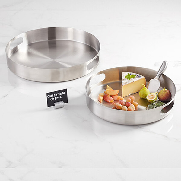 Two American Metalcraft stainless steel serving trays with fruit and cheese on a counter.