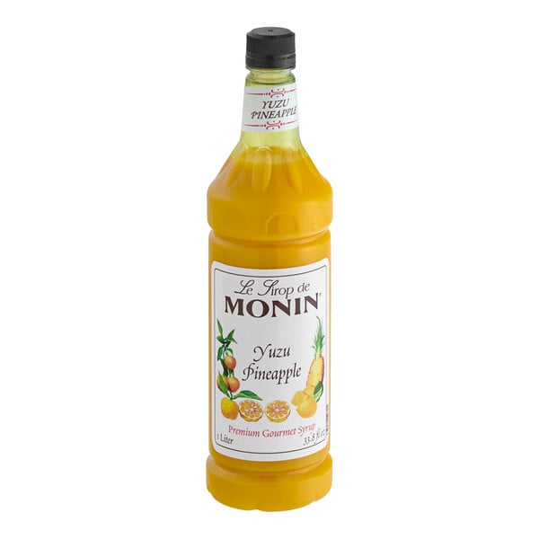 A close up of a Monin Yuzu Pineapple syrup bottle filled with yellow liquid.