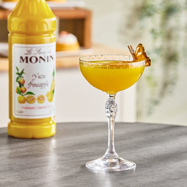 A bottle of Monin Premium Yuzu Pineapple Flavoring Syrup and a cocktail garnished with a dried pineapple slice.