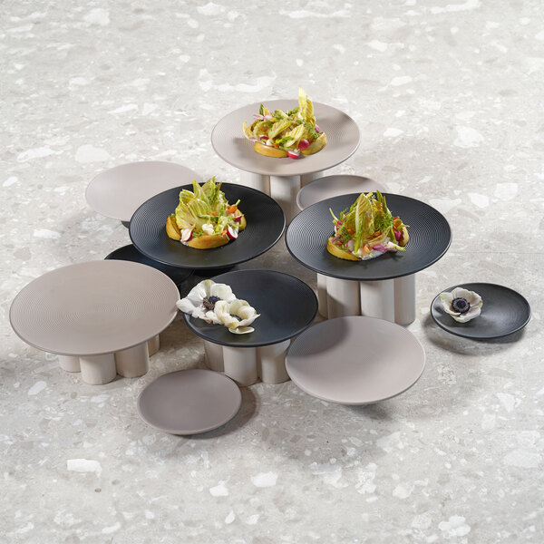 A group of Cal-Mil taupe melamine plates with food on them on a table.