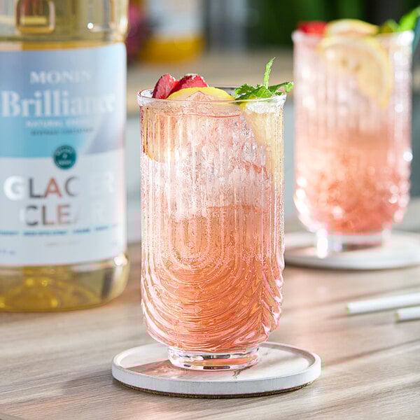 A glass with a straw and pink Monin energy drink with fruit slices and mint leaves.