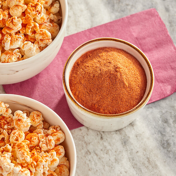 A bowl of Regal Spice Smokehouse Popcorn Seasoning next to bowls of popcorn on a marble surface.