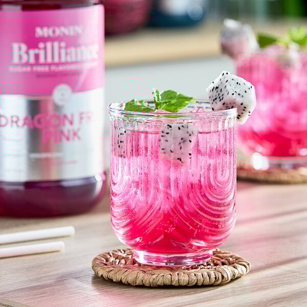 A glass of Monin Brilliance Sugar-Free Dragon Fruit Pink Natural Energy Drink with a dragon fruit garnish.