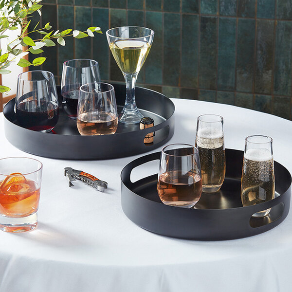 Two American Metalcraft black stainless steel serving trays with wine glasses and wine on a table.
