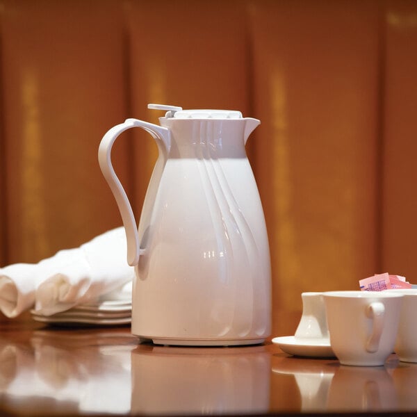 A white Service Ideas Twist 'N' Serv coffee carafe on a table with cups and saucers.