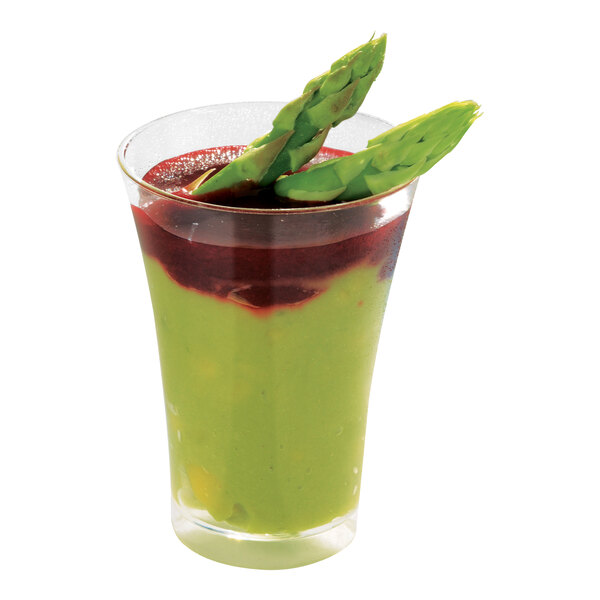 A Solia clear plastic mini flared cup filled with a red and green smoothie with asparagus as a garnish.