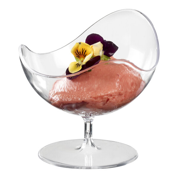 A Solia clear plastic ball chair cup with pink ice cream and flowers on a table.