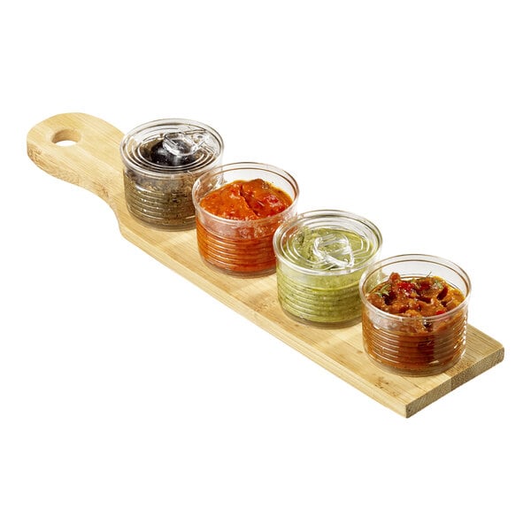A Solia clear plastic tin with a lid filled with food on a wooden board with different sauces.