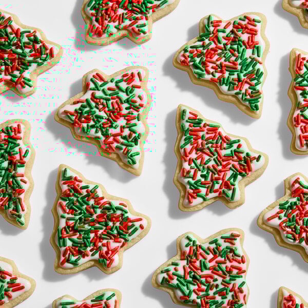 A collection of Christmas tree-shaped sugar cookies decorated with white icing and red and green holiday sprinkles.