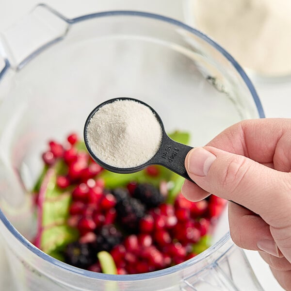 A person using a black measuring spoon to add white PB Leiner Solugel powder to a blender.