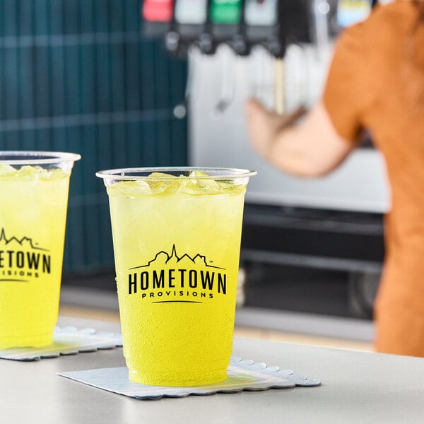 A clear plastic cup filled with a bright yellow-green citrus beverage over ice, branded with the Hometown Provisions logo.
