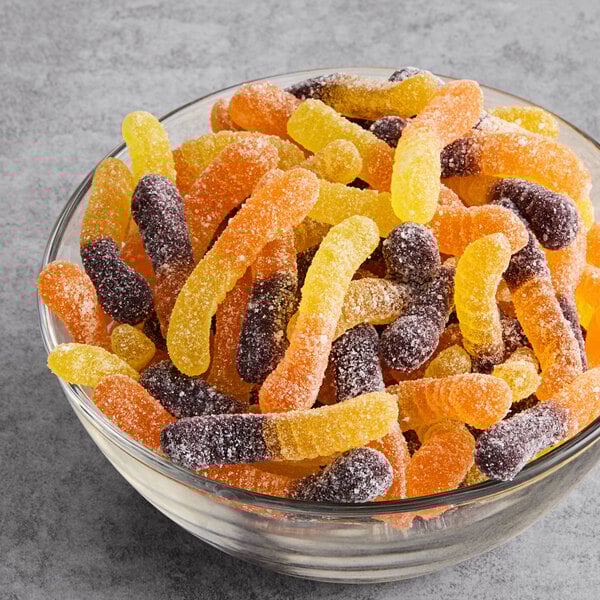 A glass bowl filled with assorted mini sour gummy worms coated in sugar.