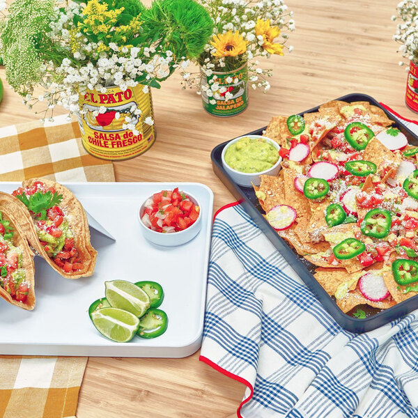 A small white straight-sided melamine ramekin filled with diced tomatoes, placed on a tray next to tacos and lime slices.