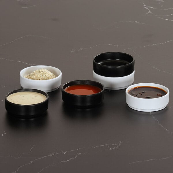 A set of small, round, white and black melamine ramekins containing various sauces and seasonings.
