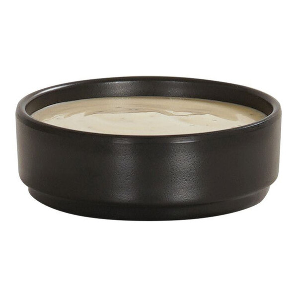 A small black melamine ramekin filled with a light-colored sauce.