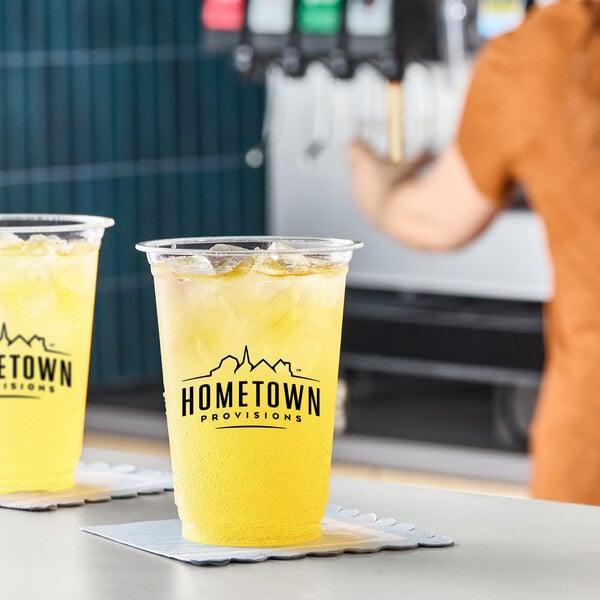 A clear plastic cup filled with iced yellow pineapple juice, branded with the Hometown Provisions logo.
