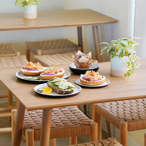 A wooden table with Cal-Mil Sophie ivory and black melamine plates and bowls of food on it.