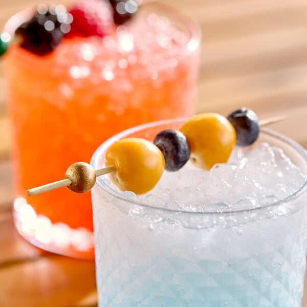 A 4 1/2 inch gold ball bamboo cocktail pick skewering fruit, placed in a glass of ice.