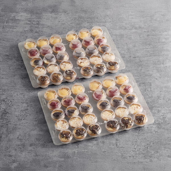 Two trays of Cuisine Innovations Mini Assorted Cheesecake on a table in a bakery display.