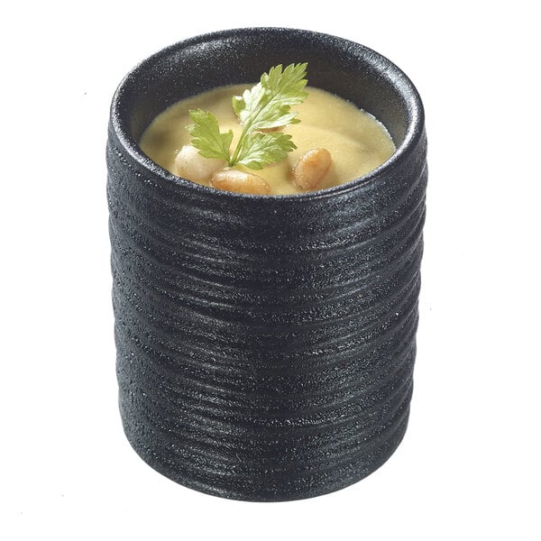 A Solia black porcelain ramekin with white sauce and a green garnish.