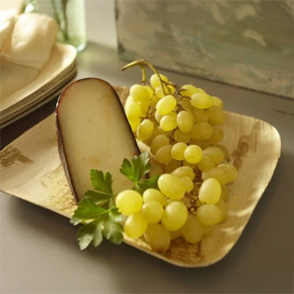 A VerTerra rectangular palm leaf plate with grapes and cheese on it.