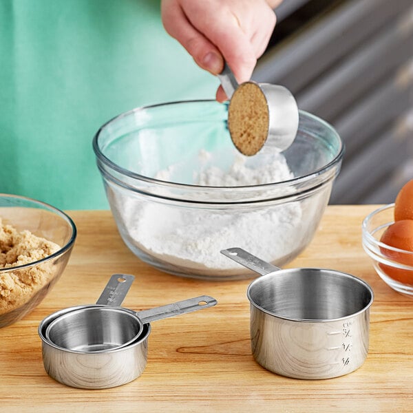 A set of four stainless steel measuring cups displayed on a wooden surface.