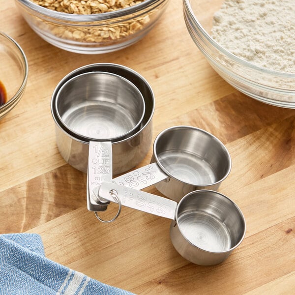 A set of four stainless steel measuring cups on a wooden surface.