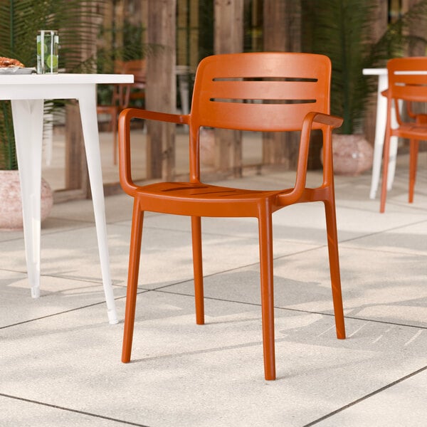 A terracotta-colored resin arm chair with a slat back design.