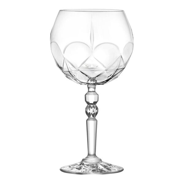 A clear, intricately cut gin and tonic glass with a faceted stem and wide bowl.