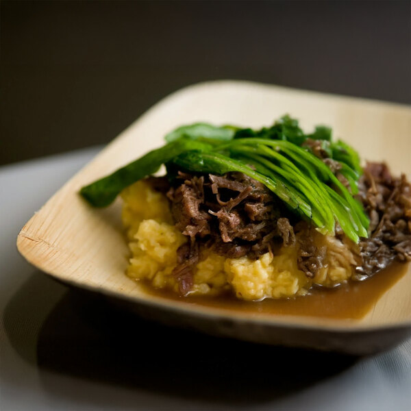 A VerTerra rectangular palm leaf bowl with meat and vegetables on a table.