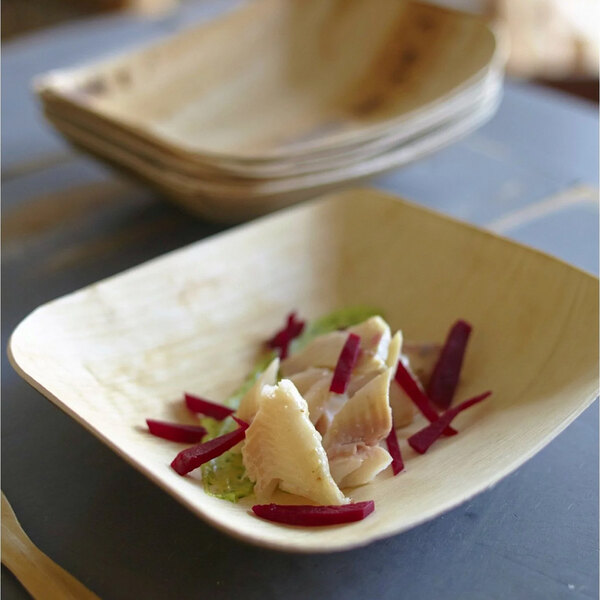 A VerTerra rectangular palm leaf bowl filled with food on a table.