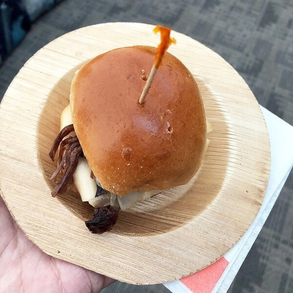 A hand holding a sandwich on a VerTerra round palm leaf plate.