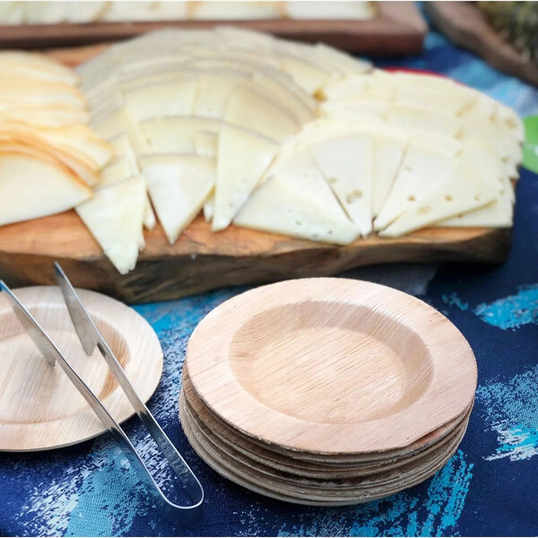 A table set with VerTerra palm leaf plates holding sliced cheese and tongs.