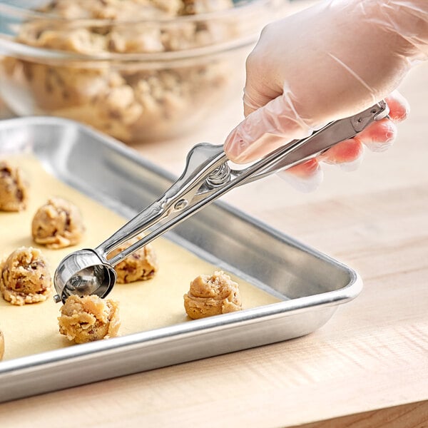A stainless steel squeeze handle disher being used to portion cookie dough onto a baking sheet.