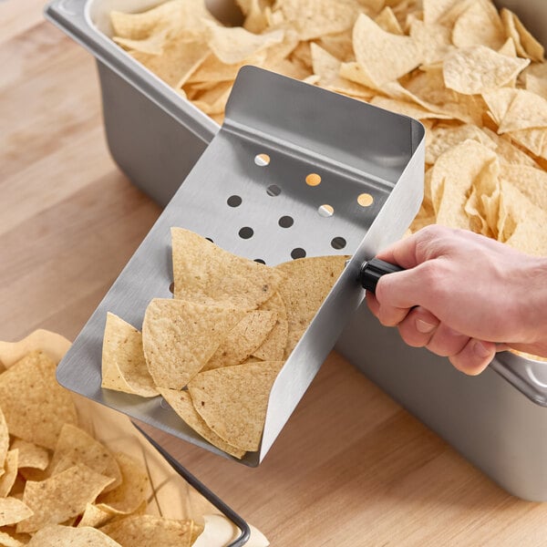 A stainless steel chip scoop with a black handle being used to serve tortilla chips.