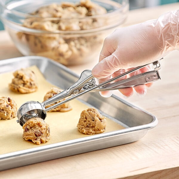 A stainless steel squeeze handle disher being used to portion cookie dough onto a baking sheet.