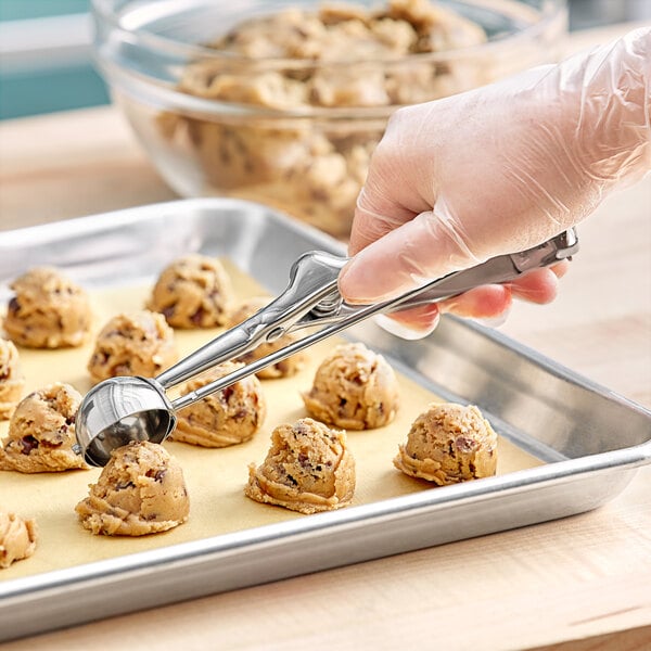 A stainless steel squeeze handle disher being used to portion cookie dough onto a baking sheet.