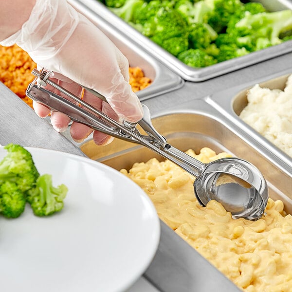A stainless steel round squeeze handle disher being used to serve macaroni and cheese from a food tray.