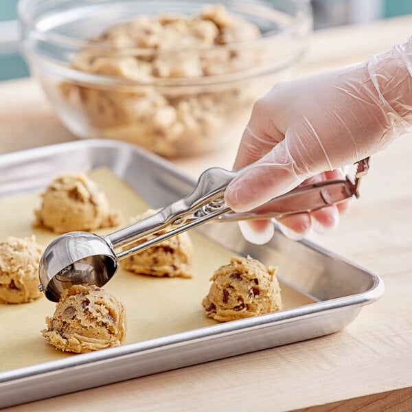 A stainless steel squeeze handle disher being used to scoop cookie dough onto a baking sheet.