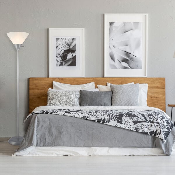 A silver 72-inch floor lamp with a white plastic shade and an on/off rotary switch on the shade, placed next to a bed in a modern bedroom.