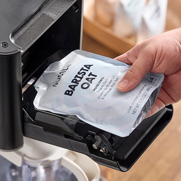 A hand holding a bag of Numilk Barista Oat Milk Concentrate.